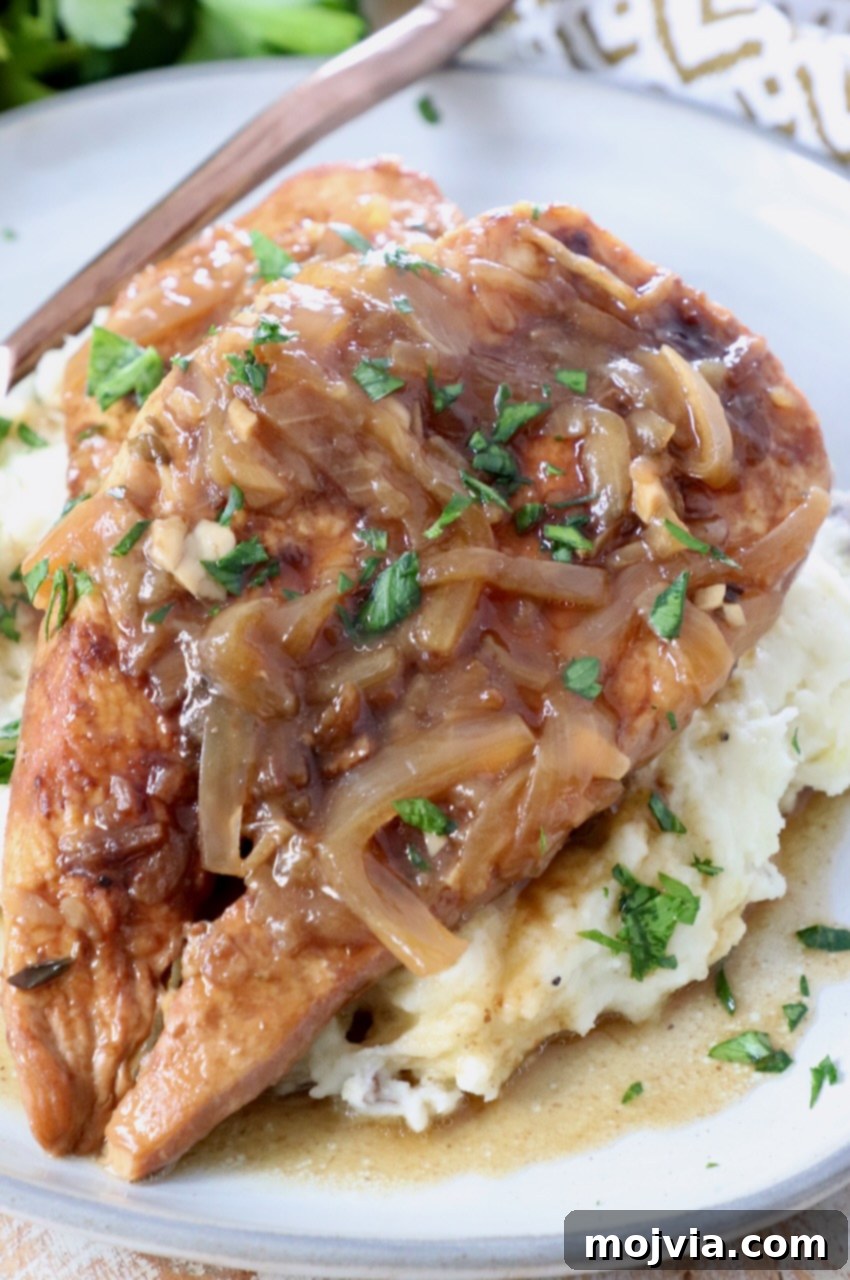 Rich Slow Cooker French Onion Chicken 11 Cooked French Onion Chicken breasts with caramelized onion gravy on top of mashed potatoes on a plate.