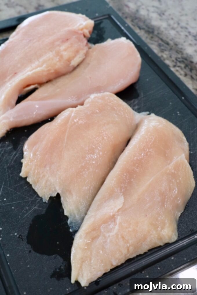 Rich Slow Cooker French Onion Chicken 4 Raw chicken breasts sliced in half on a cutting board.