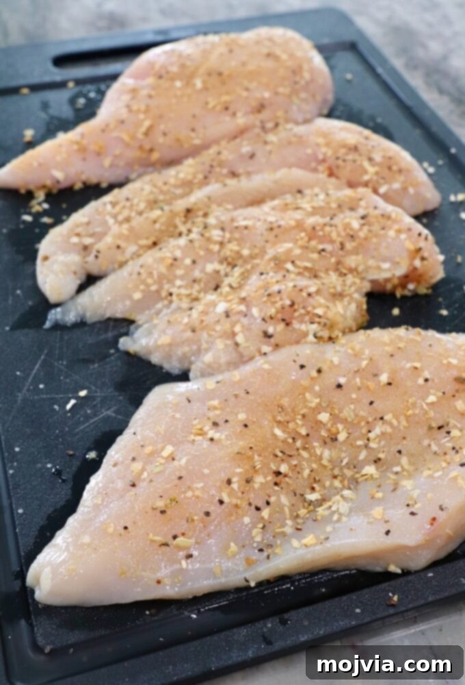 Rich Slow Cooker French Onion Chicken 5 Seasoned raw chicken breasts, sliced in half, on a cutting board.