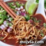 cooked ramen noodles lifted up with chopsticks in bowl of birria broth