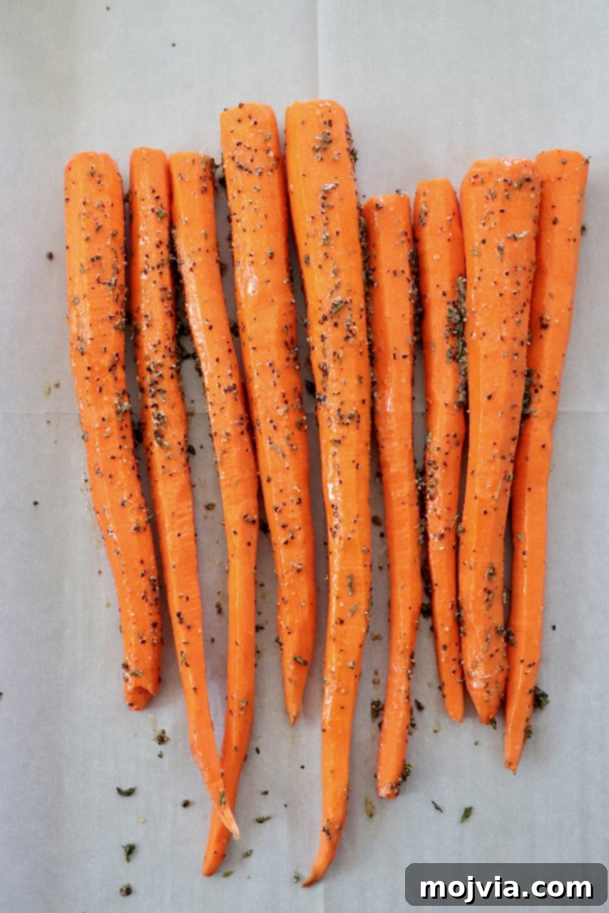 seasoned carrots arranged on a parchment lined baking sheet, ready for roasting