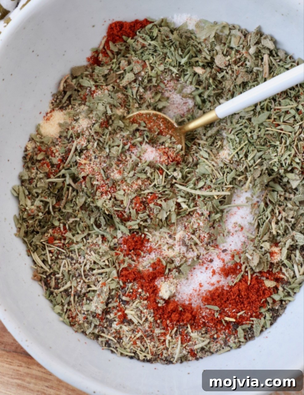 Close-up of freshly mixed turkey seasoning in a bowl with a small spoon, showcasing the rich colors and textures of the herbs and spices.