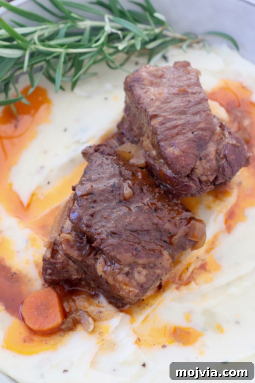 Melt-Off-The-Bone Guinness Short Ribs 2 braised short ribs on top of mashed potatoes in bowl with fresh rosemary sprigs