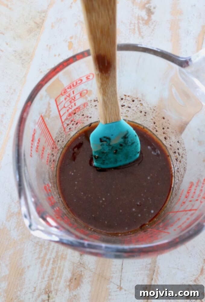 Close-up of honey butter glaze in a glass measuring cup with a spatula, ready to be applied.
