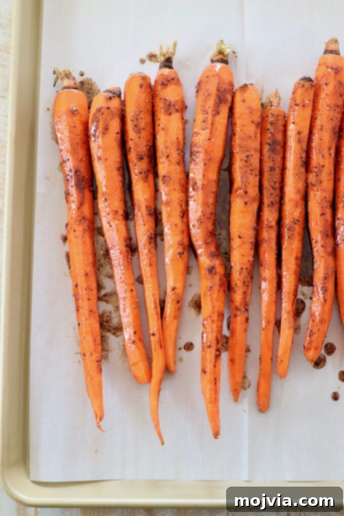 Honey glazed carrots arranged on a parchment-lined baking sheet, prepared for roasting.