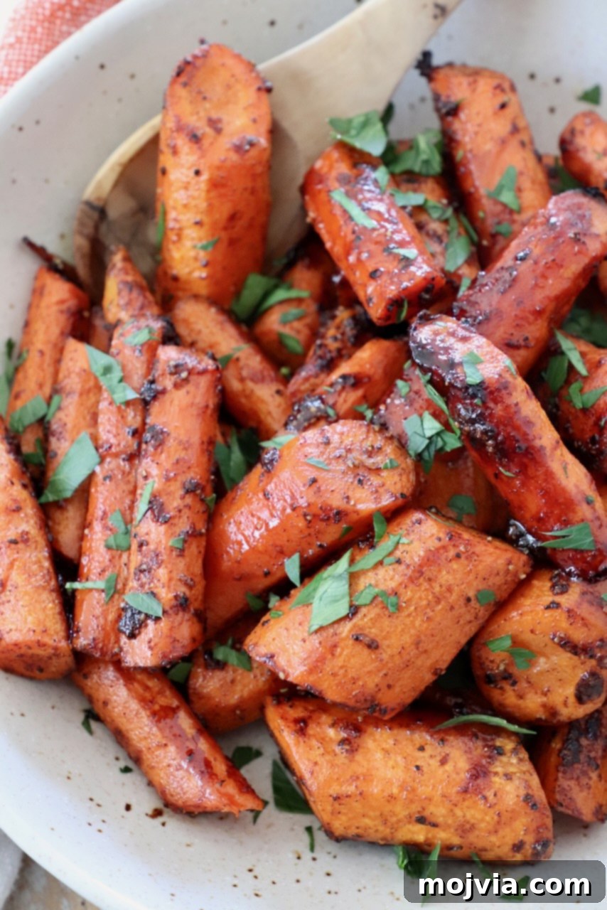Sliced honey glazed roasted carrots in a white bowl with a serving spoon, ready to enjoy.