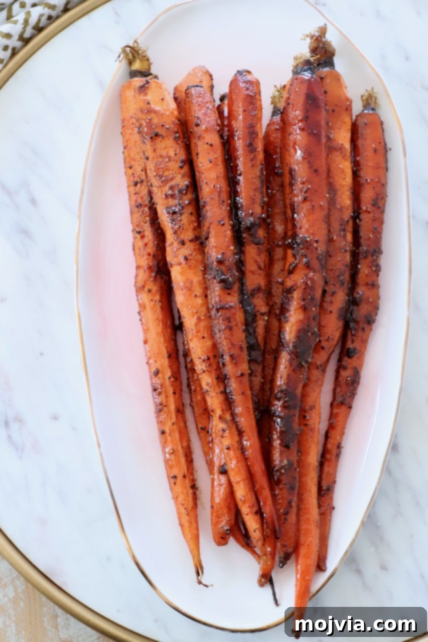 Beautifully glazed roasted carrots, stacked artfully on a white plate, showcasing their perfect texture and sheen.