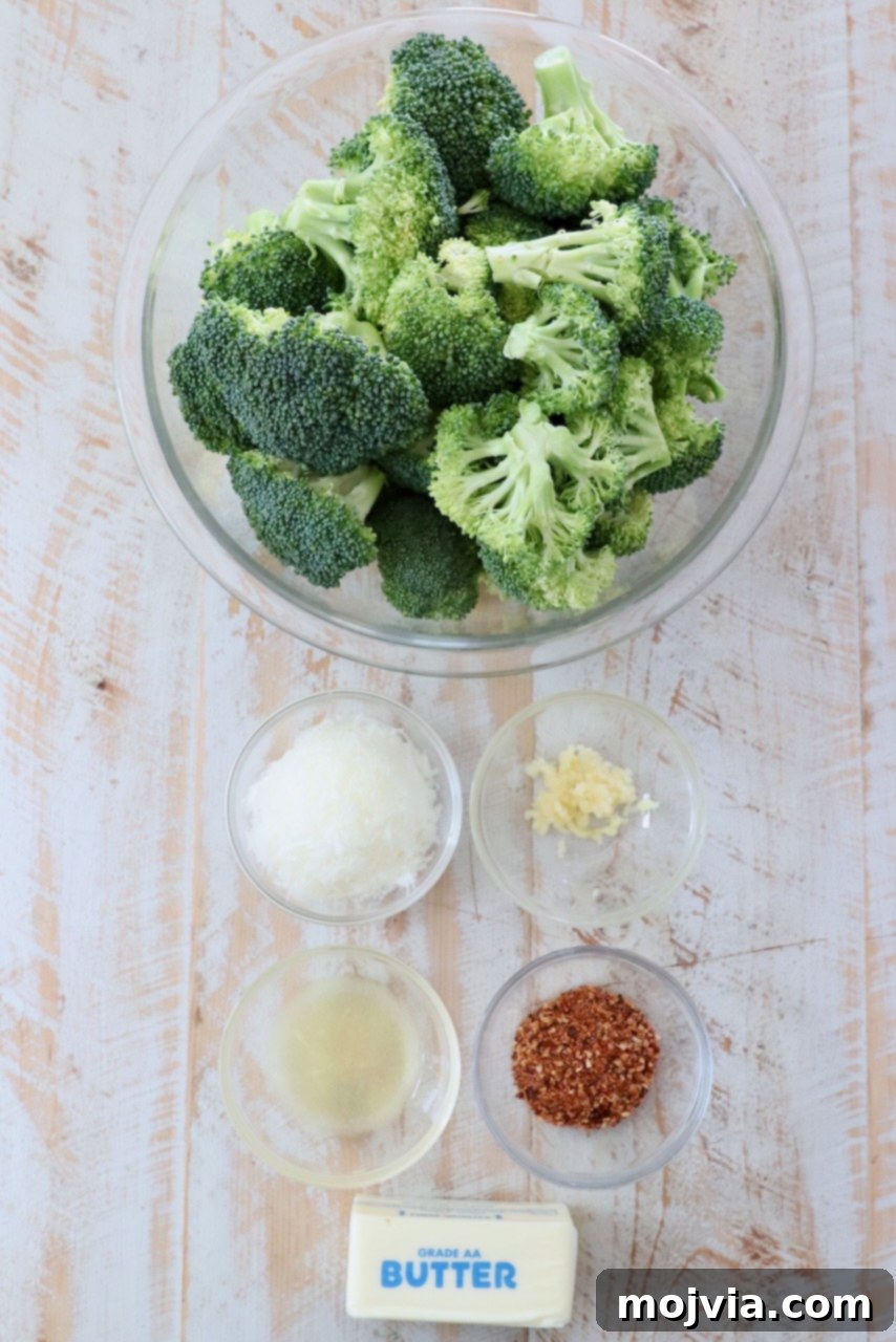 Crispy Smashed Broccoli 3 Assortment of fresh ingredients for smashed broccoli, including broccoli florets, butter, lemons, garlic, steak seasoning, and Parmesan cheese on a white wooden board