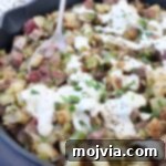 steak and potato hash in skillet topped with cheese sauce