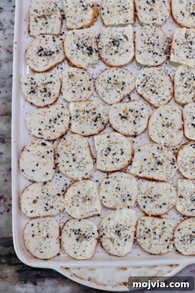 Toasted Bagel Crisps 5 Seasoned bagel slices meticulously arranged in a single layer on a baking sheet, prepped for the oven.