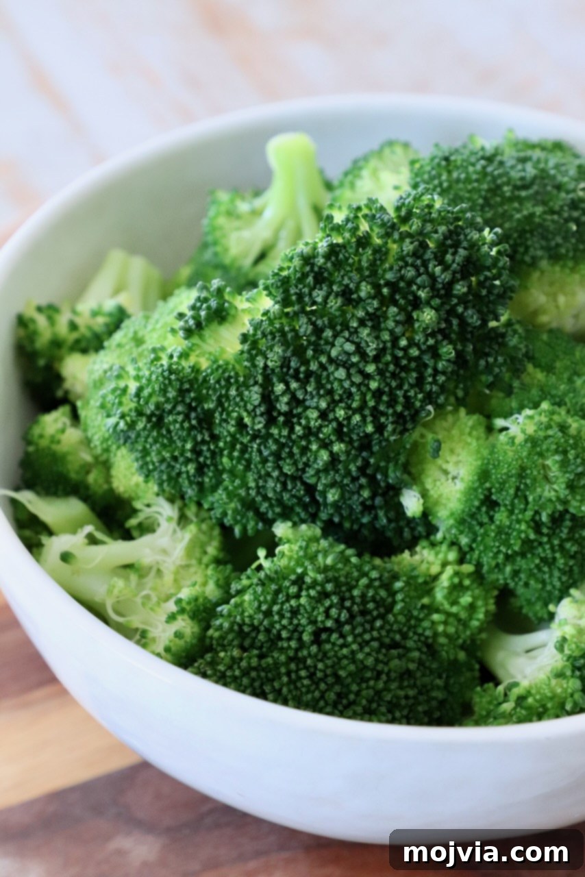 Flawless Steamed Broccoli in Minutes 2 Freshly steamed broccoli florets in a white bowl, ready to serve, highlighting its vibrant green color and tender appearance.