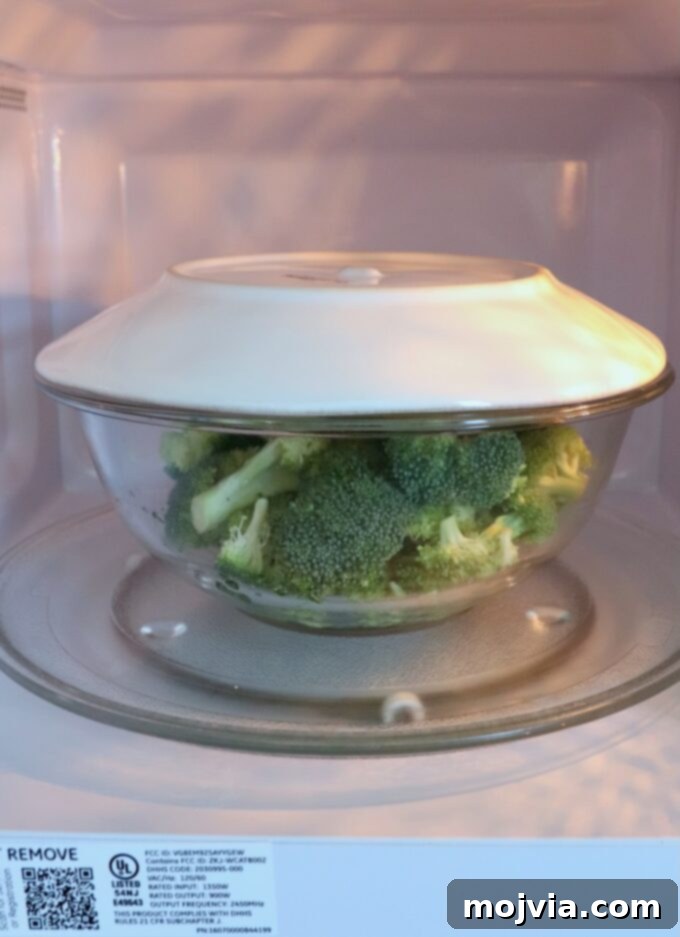Flawless Steamed Broccoli in Minutes 3 Broccoli florets in a glass bowl, covered with a microwave-safe plate, prepared for microwave steaming.