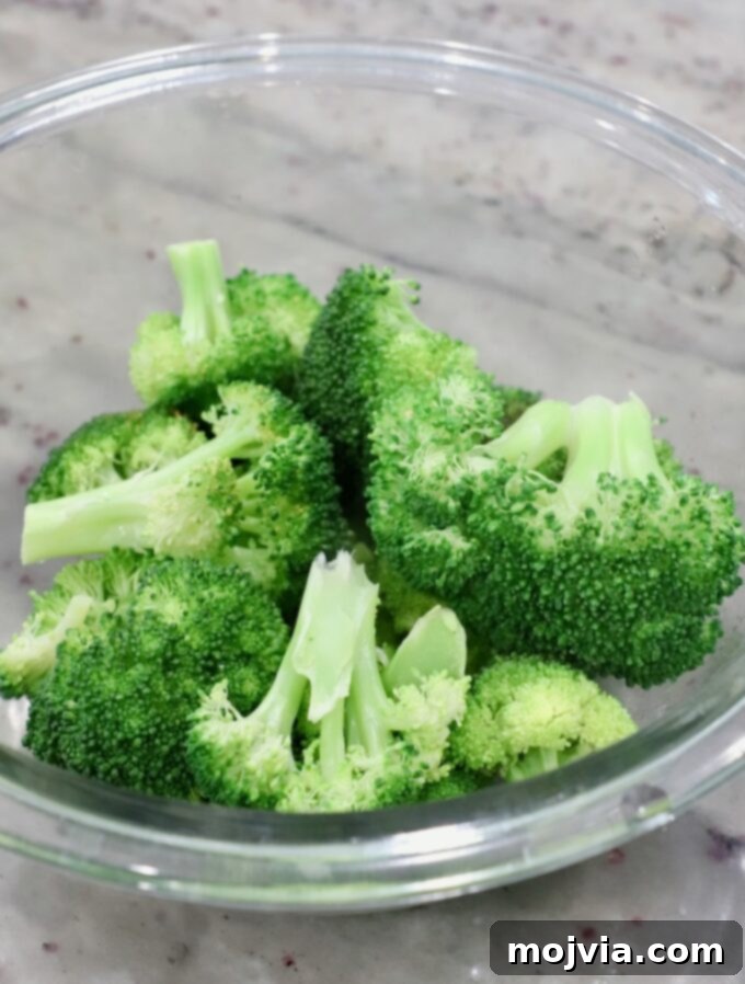 Flawless Steamed Broccoli in Minutes 4 Perfectly steamed broccoli florets resting in a clear glass bowl, showcasing their bright green color and tender texture.