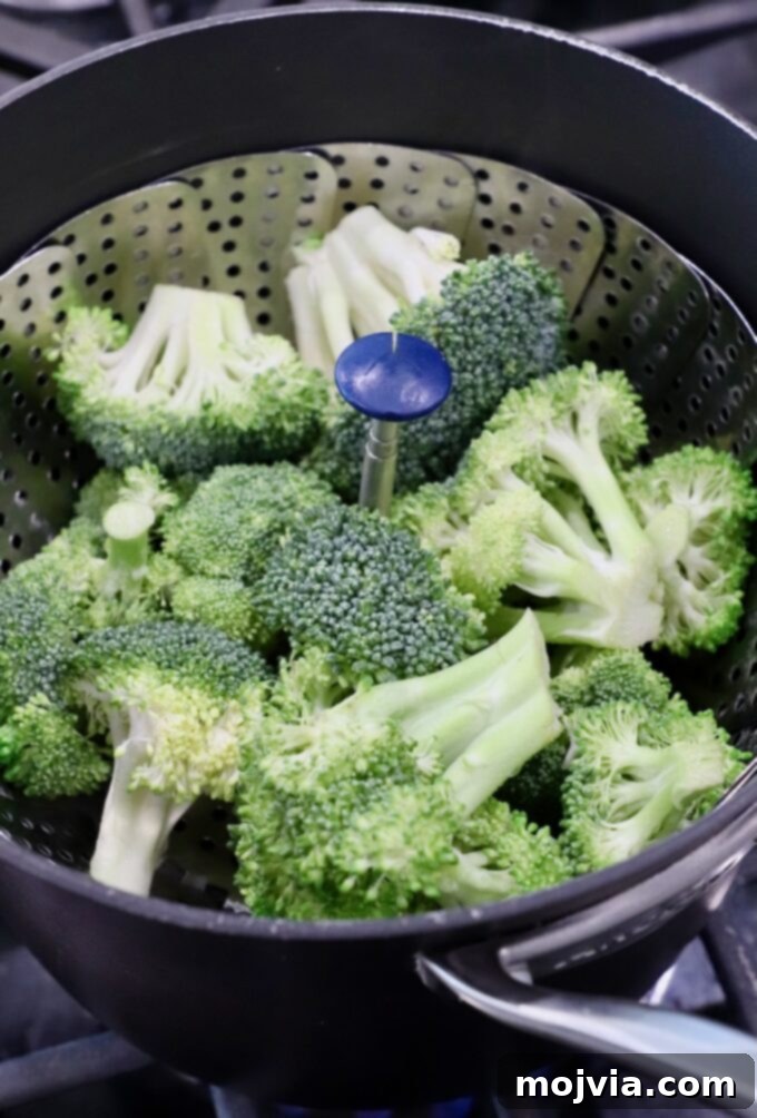 Flawless Steamed Broccoli in Minutes 5 Broccoli florets neatly arranged in a metal steamer basket, placed inside a pot on the stovetop, ready for steaming.