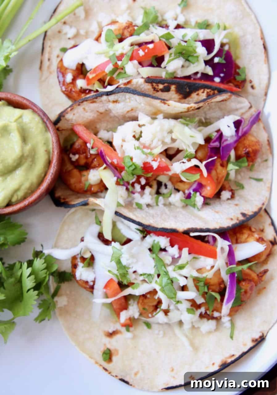 Zesty Grilled Shrimp Tacos with Creamy Avocado Salsa 3 Overhead image of three shrimp tacos on plate with a side of avocado salsa