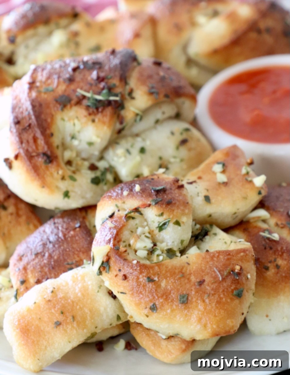 Freshly baked garlic knots on a white plate, served with a small bowl of marinara sauce for dipping.