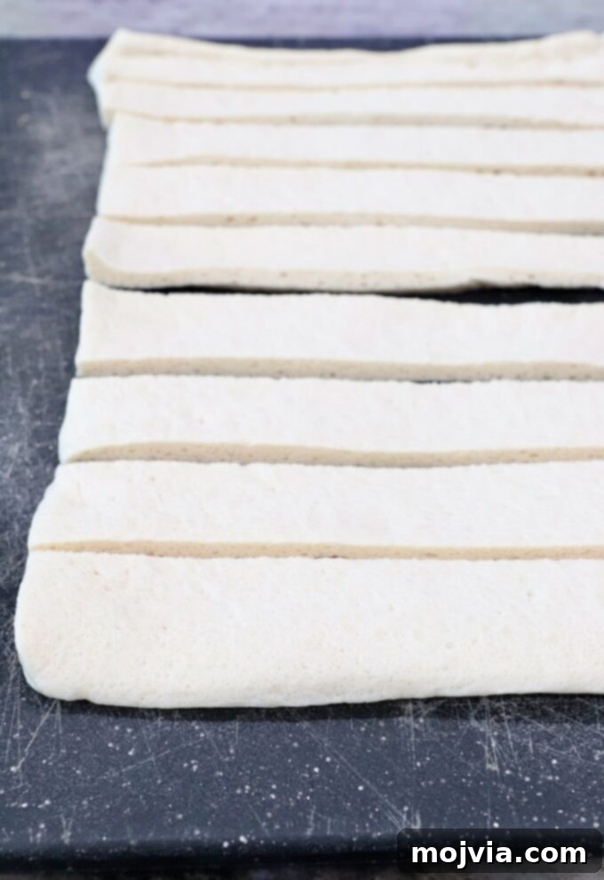Sliced pizza dough strips on a wooden cutting board, ready to be tied into knots.