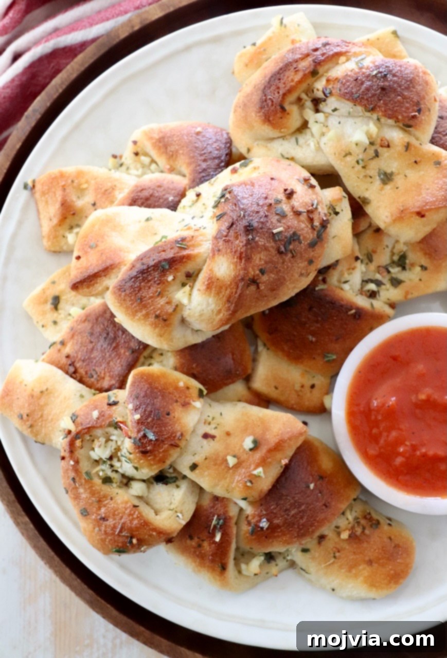 A stack of golden brown garlic knots on a plate, with a small bowl of rich red marinara sauce on the side, ready for dipping.