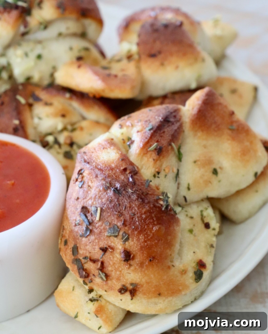 Freshly baked garlic knots on a white plate, positioned next to a small bowl filled with savory marinara sauce, ready for a delicious dip.