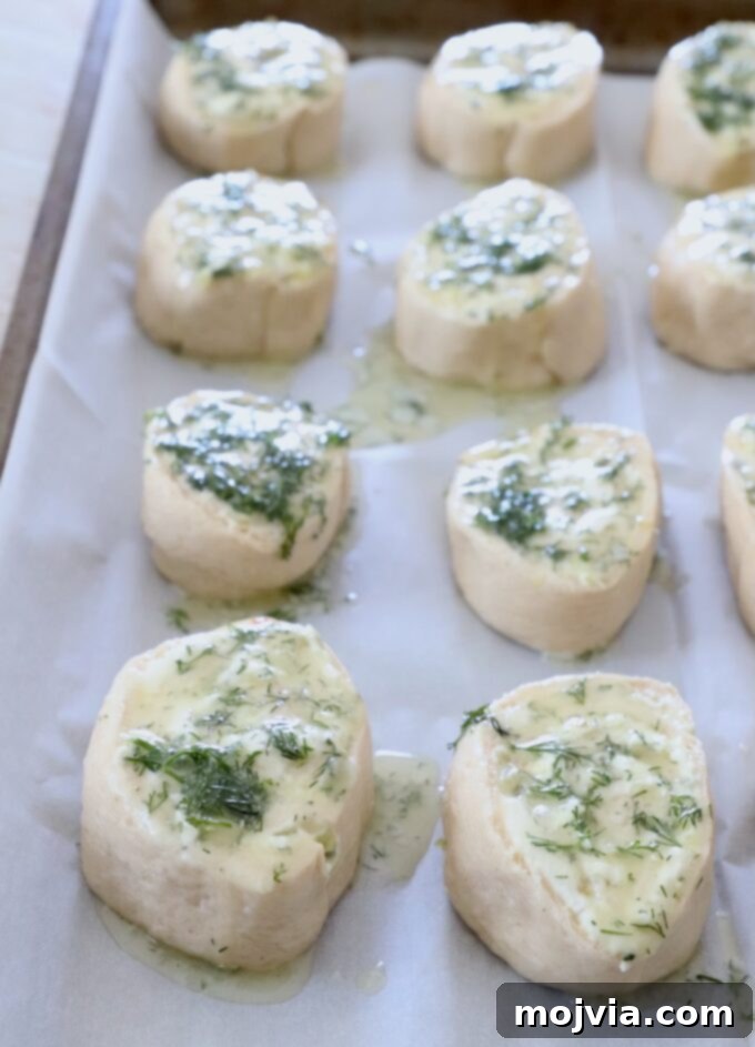 uncooked creamy pickle rolls on parchment-lined baking sheet topped with dill butter