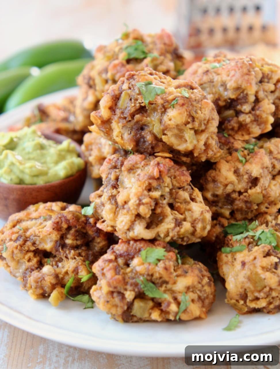 Platter of chorizo sausage balls, beautifully arranged with a small wooden bowl of creamy avocado dipping sauce beside them.