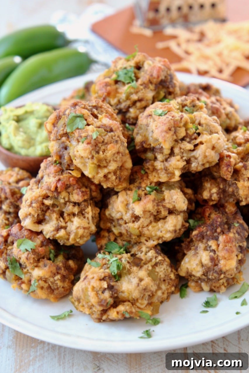 A vibrant plate of Mexican Chorizo Bisquick Sausage Balls, garnished with fresh jalapenos and shredded cheddar cheese, with creamy avocado sauce nearby.