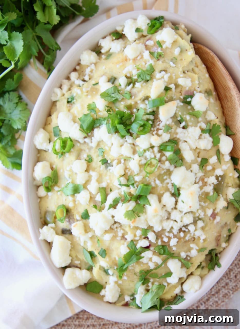 Mashed Mexican Potatoes in a bowl with a wooden spoon, topped with queso fresco and fresh cilantro