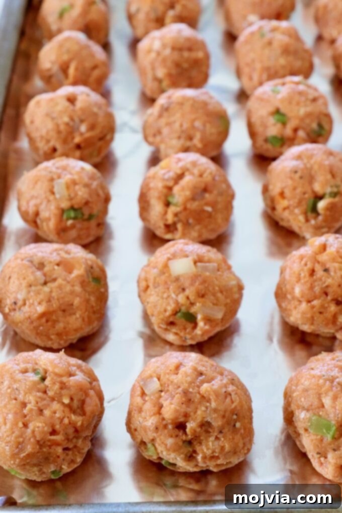 Zesty Buffalo Chicken Poppers 7 Uncooked buffalo chicken meatballs neatly arranged on a foil-lined baking sheet, ready for broiling