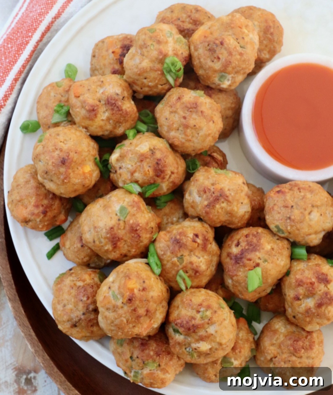 Zesty Buffalo Chicken Poppers 8 Cooked buffalo chicken meatballs on a plate with a small side of buffalo sauce for dipping