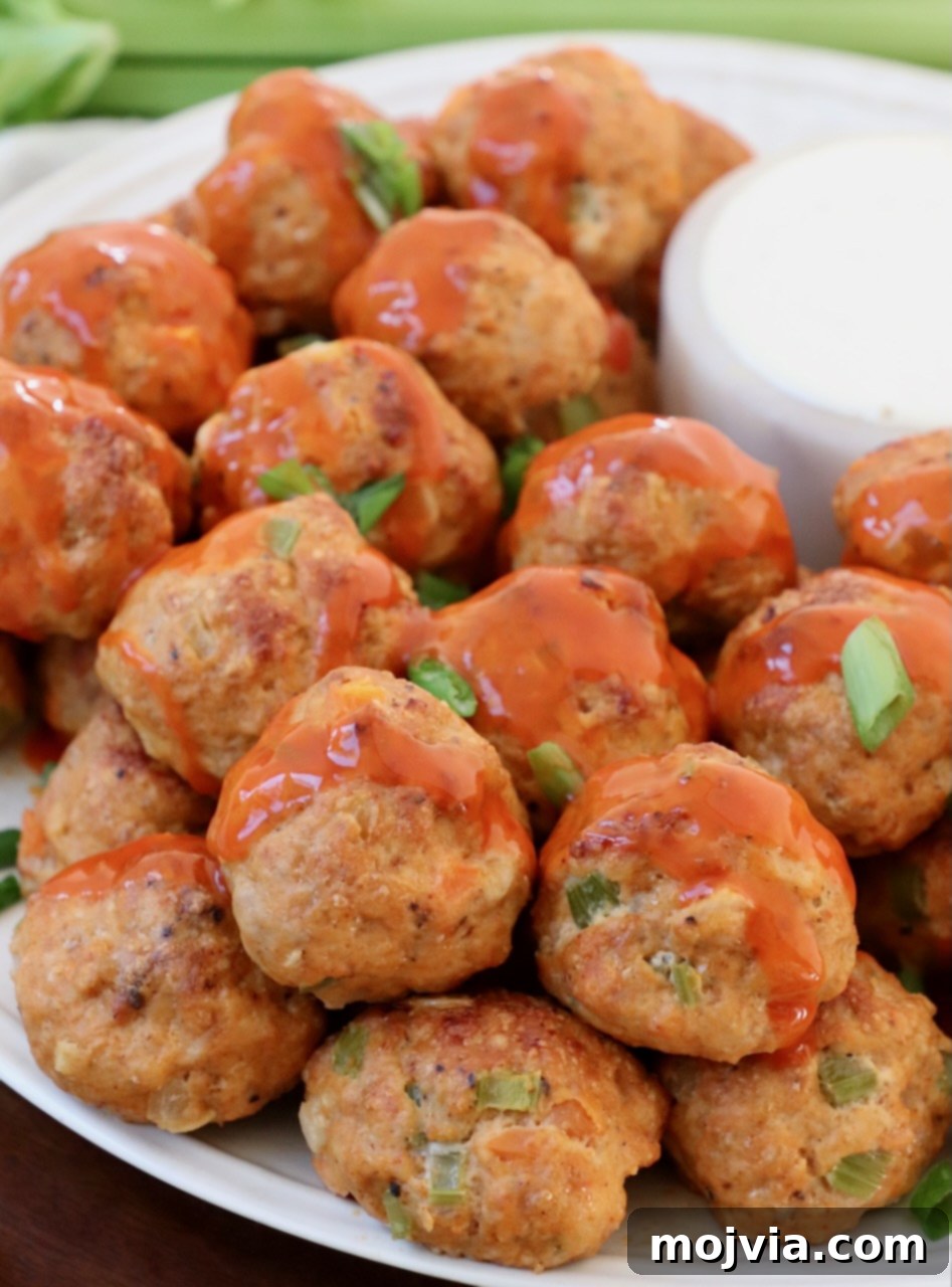 Zesty Buffalo Chicken Poppers 10 Buffalo chicken meatballs on a white plate, generously drizzled with spicy buffalo sauce
