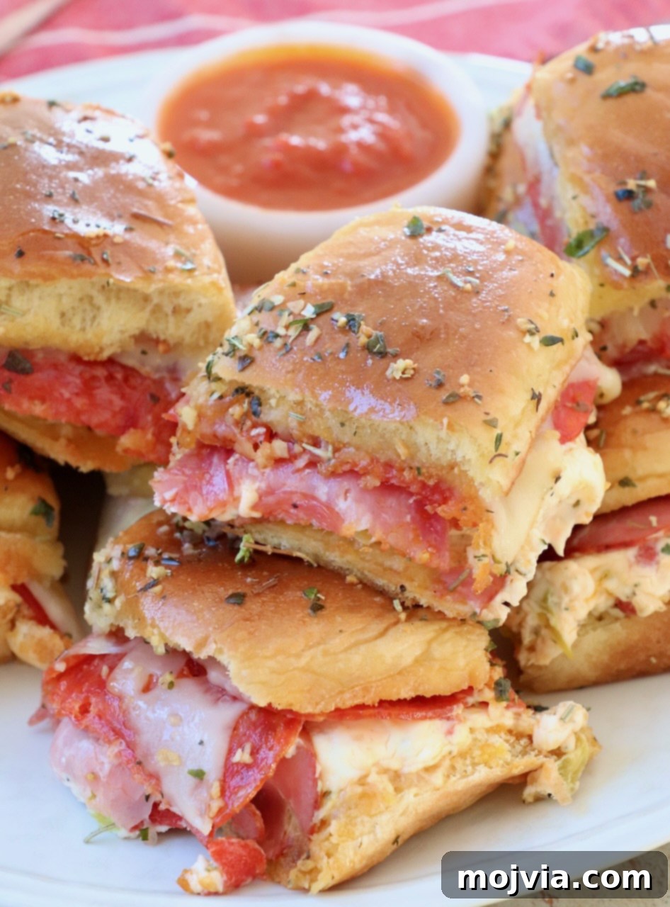 Hot Italian Sliders, stacked neatly on a plate, with a small bowl of rich marinara sauce for dipping on the side. The melted cheese and golden rolls are visible.