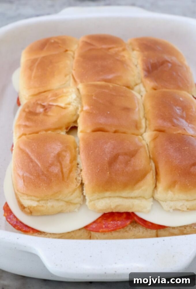 The assembled Italian sub sliders in a casserole dish, with the top half of the rolls placed back on, before adding the butter topping.