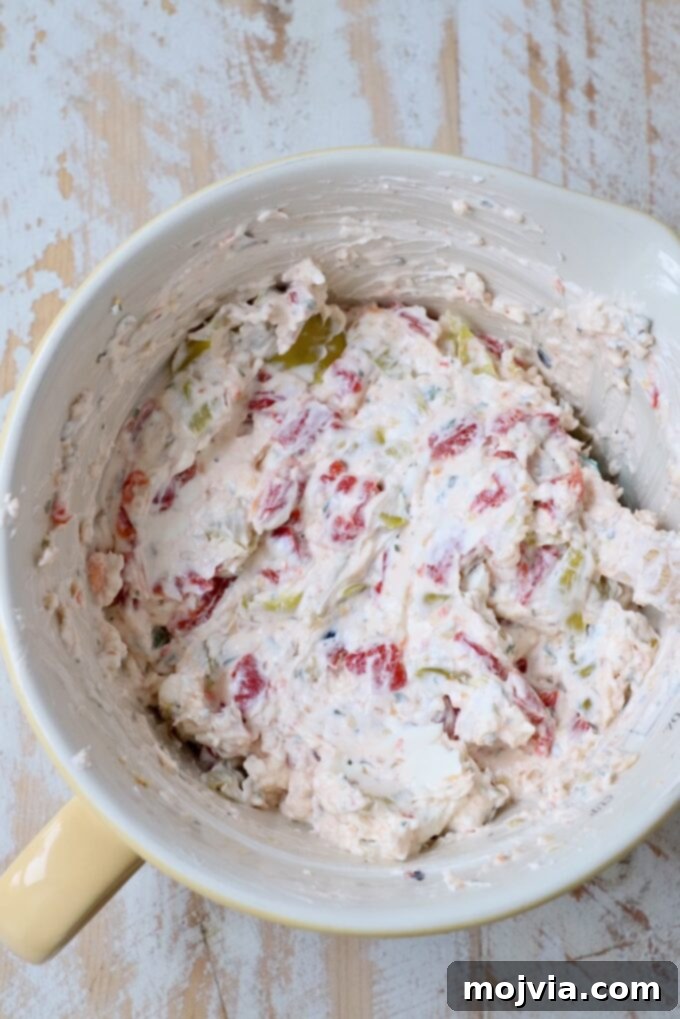 Cream cheese mixed with roasted red peppers, sliced pepperoncinis, and Italian seasoning in a bowl, ready to be spread.