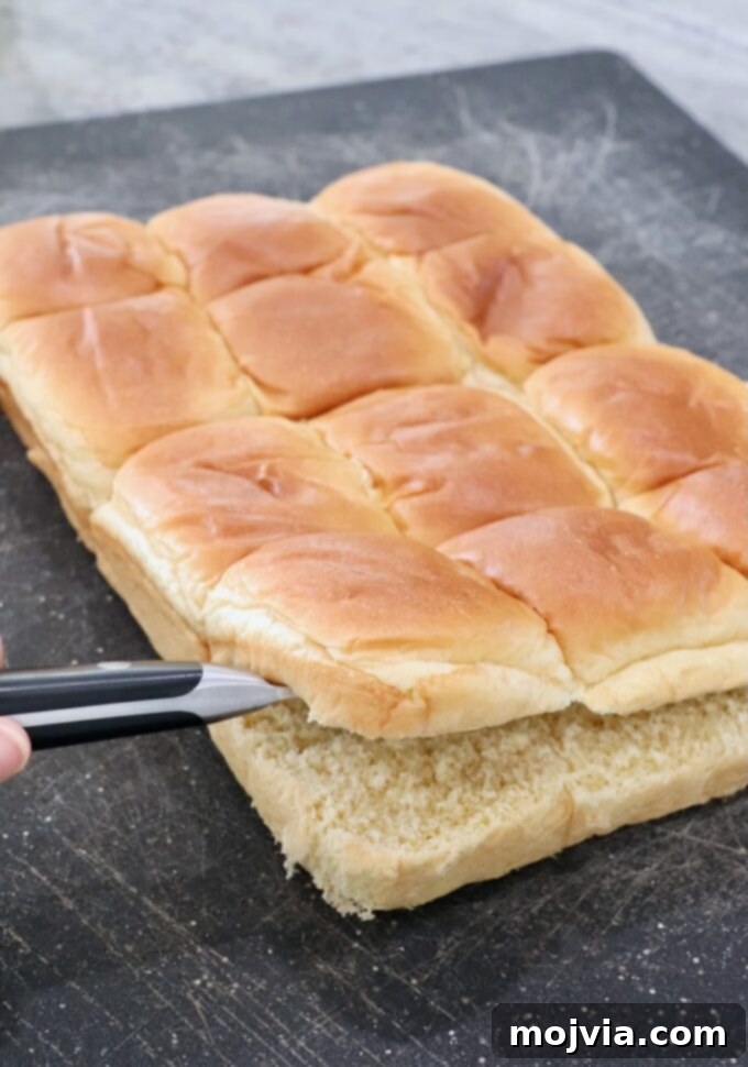 Brioche rolls, still connected, sliced neatly through the middle with a serrated knife on a cutting board.
