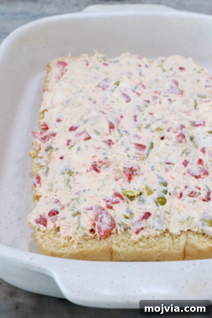 The bottom half of the brioche rolls placed in a casserole dish, topped with a generous layer of the seasoned cream cheese mixture.