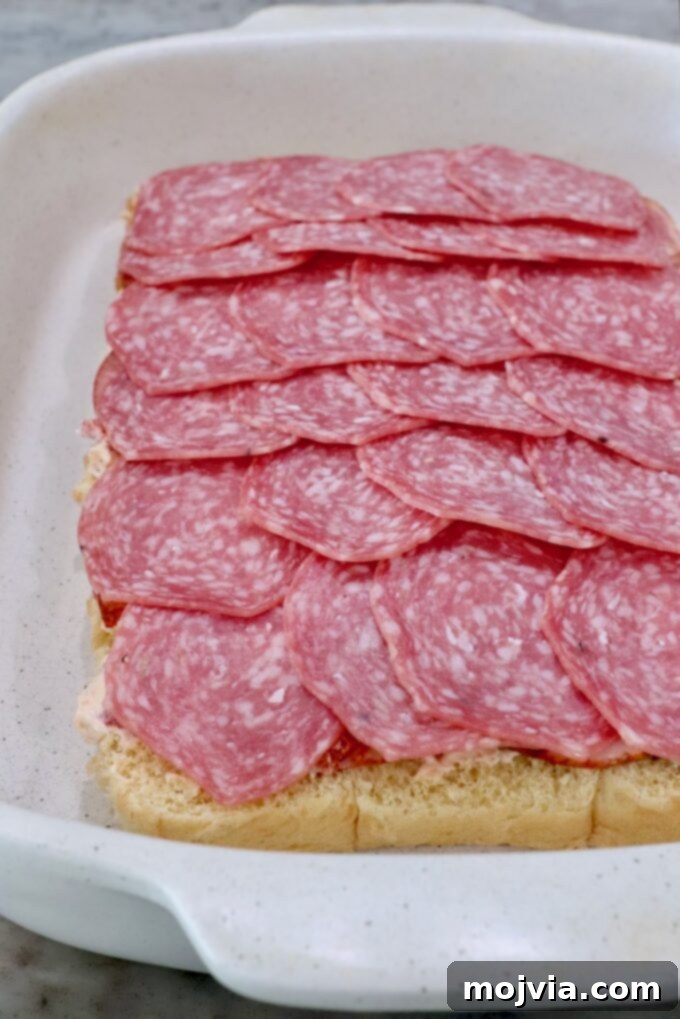 A layer of sliced salami arranged over the capocollo and cream cheese mixture in the casserole dish.