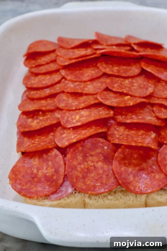 Sliced pepperonis spread over the layers of salami and capocollo in the casserole dish, completing the deli meat stack.