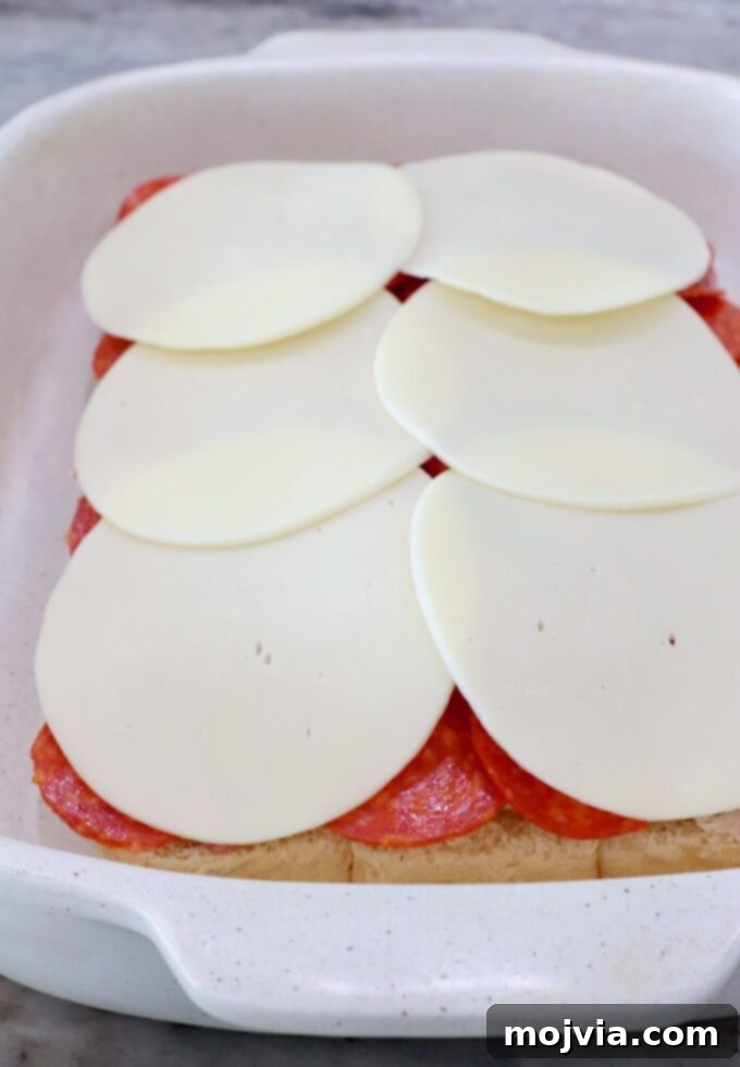 A top layer of provolone cheese slices covering all the deli meats and cream cheese in the casserole dish, ready for the top bun.