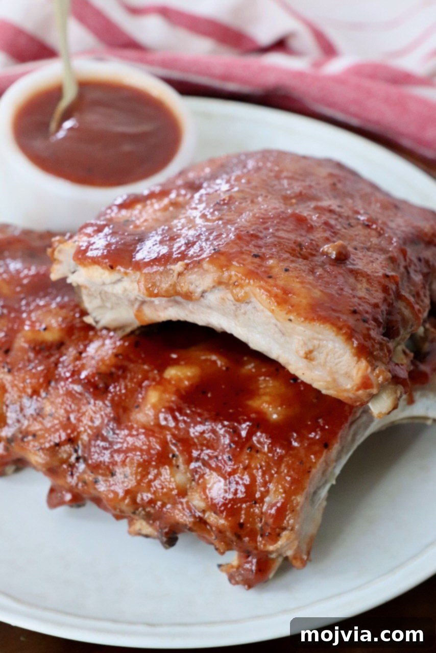 cooked baby back ribs stacked up on a plate with a small bowl of bbq sauce on the side, showing the delicious results of a good dry rub.