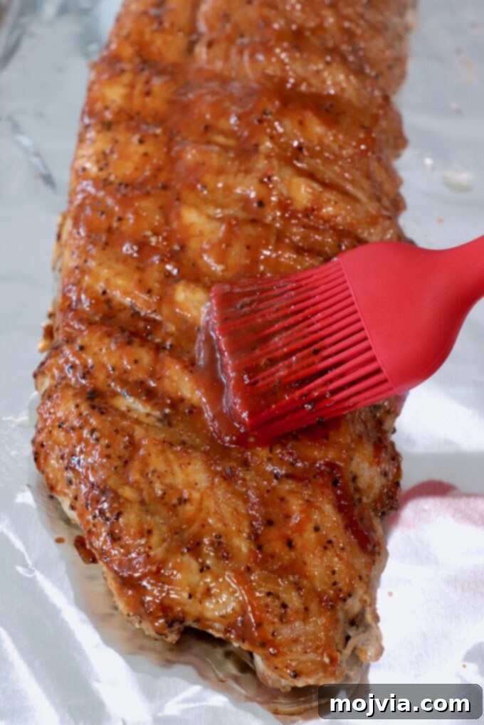 Fall Off The Bone Instant Pot Ribs 7 cooked rack of ribs on foil-lined baking sheet, brushed with bbq sauce