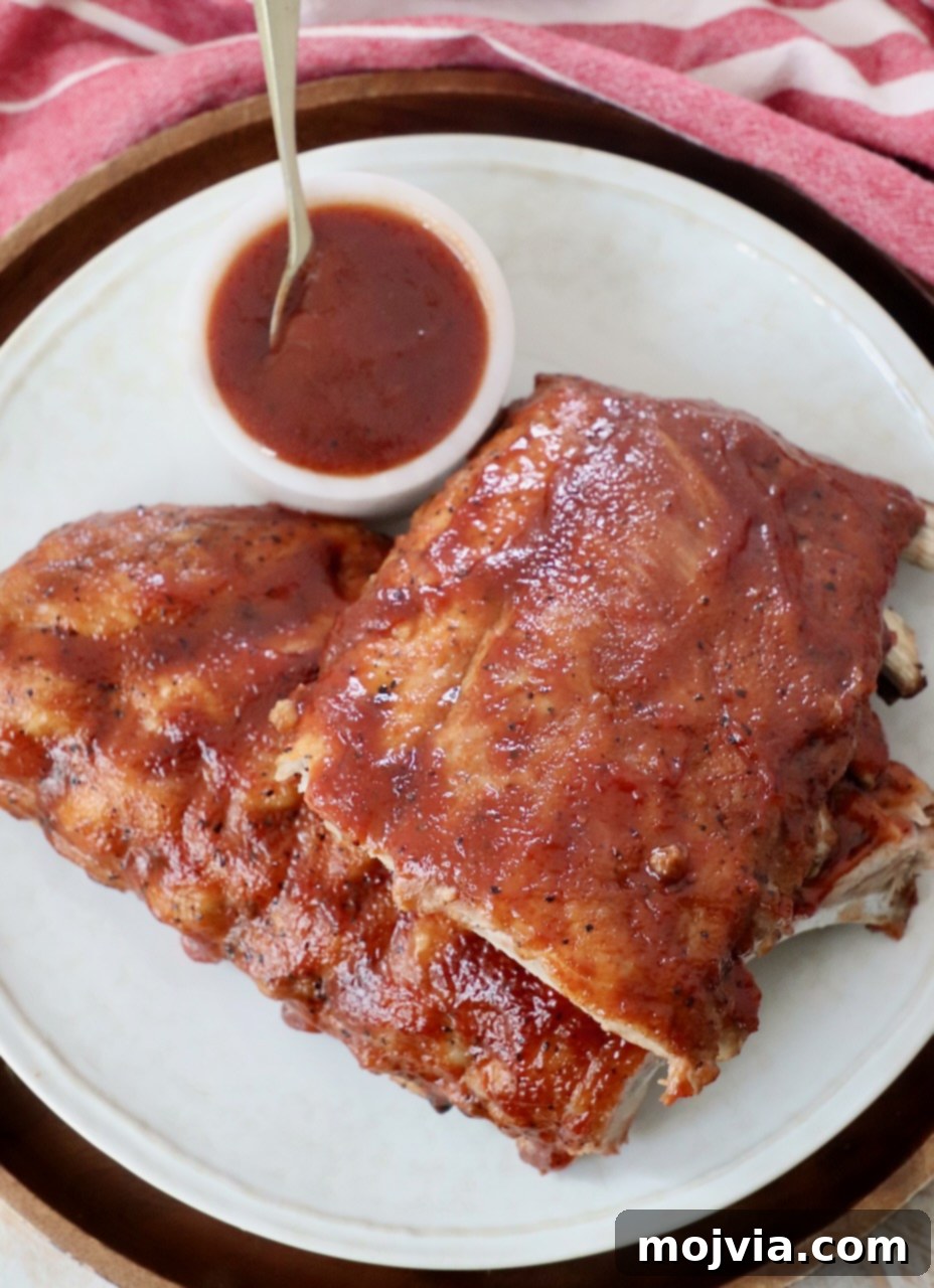 Fall Off The Bone Instant Pot Ribs 10 rack of cooked baby back ribs, cut in half on plate with a small bowl of bbq sauce