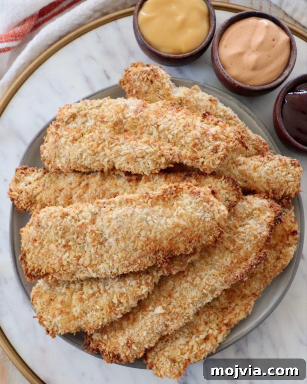 Golden Crispy Air Fryer Chicken 2 cooked, breaded chicken tenders stacked up on plate with small bowls of sauce on the side