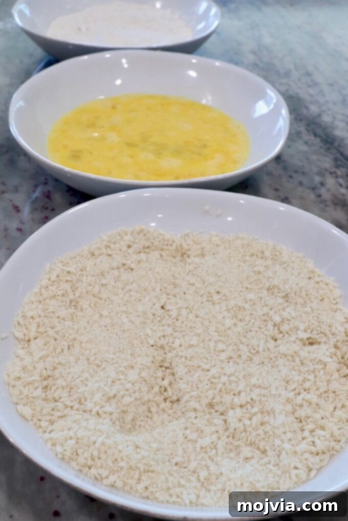 Golden Crispy Air Fryer Chicken 4 three bowls with breadcrumbs in one bowl, whisked eggs in another bowl and flour in the third bowl