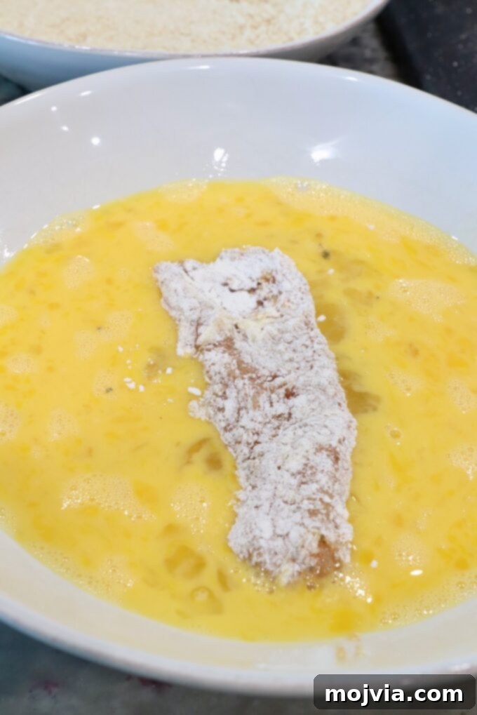 Golden Crispy Air Fryer Chicken 6 strip of seasoned flour-coated chicken in a bowl of whisked eggs