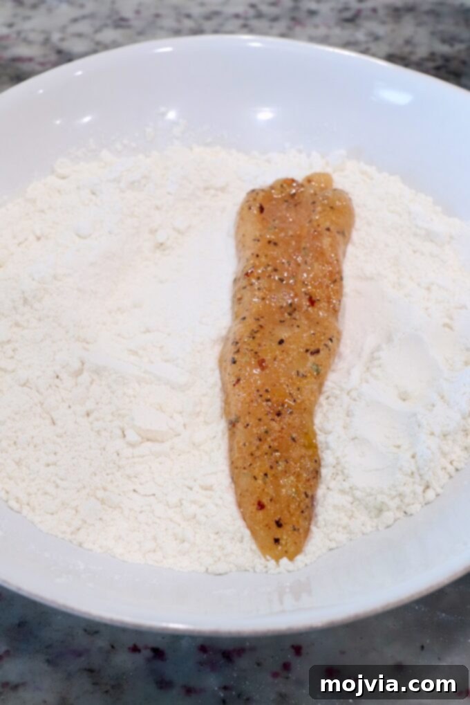 Golden Crispy Air Fryer Chicken 7 strip of seasoned chicken in bowl of flour