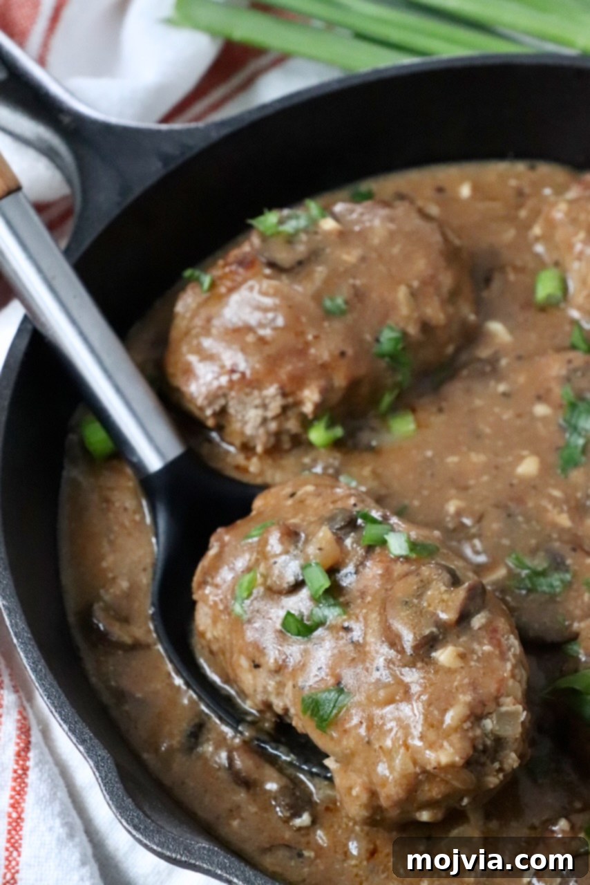 Homemade Salisbury Steak lifted from a skillet with a serving spoon, showcasing its rich mushroom gravy.