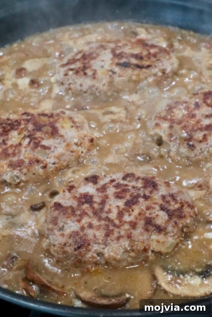 Salisbury steaks submerged in a delicious mushroom gravy, simmering gently on the stovetop, absorbing all the rich flavors.