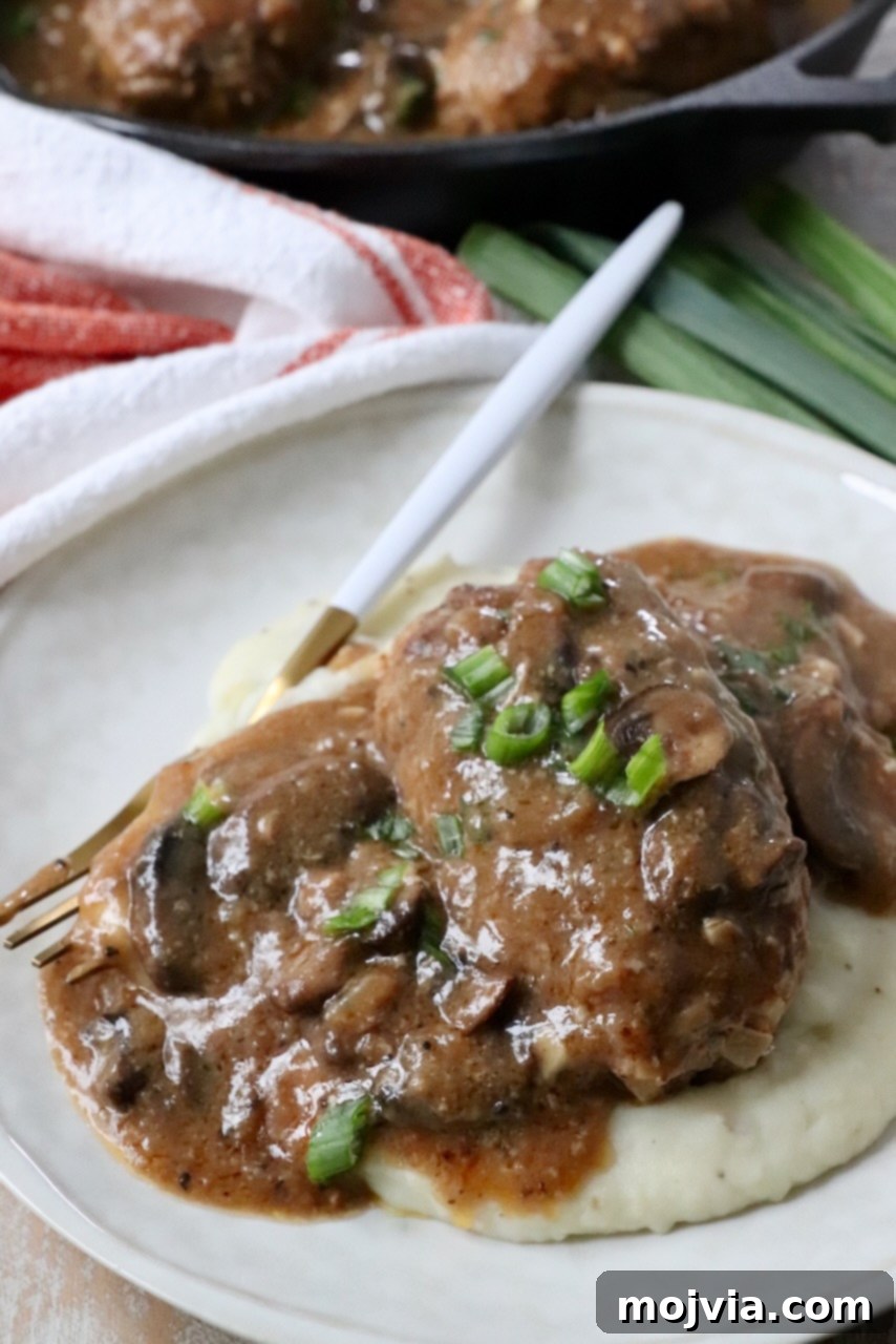 A plated Salisbury Steak, generously covered with mushroom gravy and served alongside creamy mashed potatoes, ready to be enjoyed.