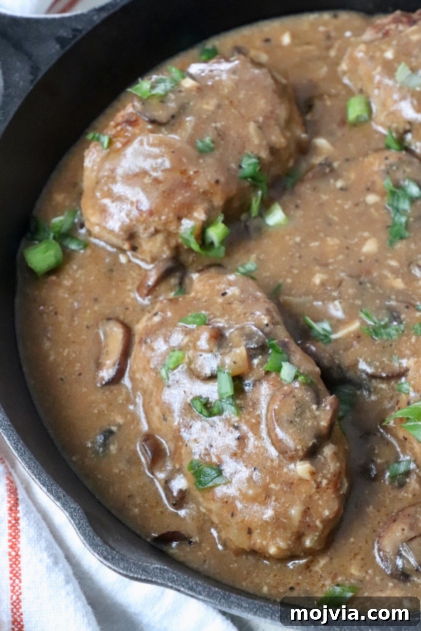 Salisbury steak generously covered in mushroom gravy, simmering beautifully in a large skillet on the stovetop.
