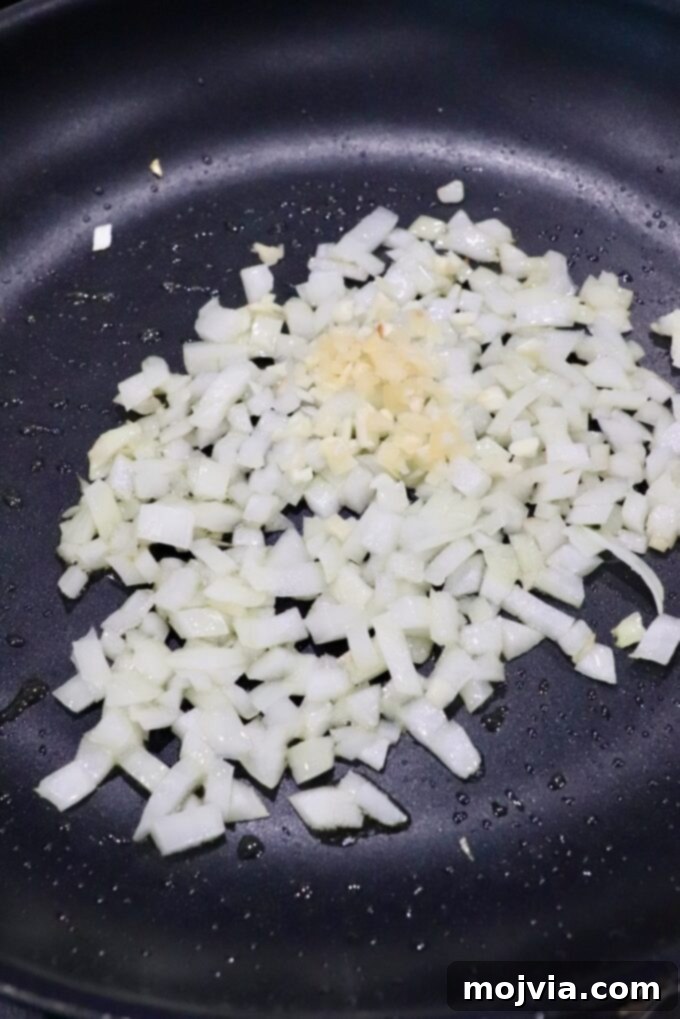 Diced onions and garlic being sautéed in a skillet, softening to release their aroma and flavor.